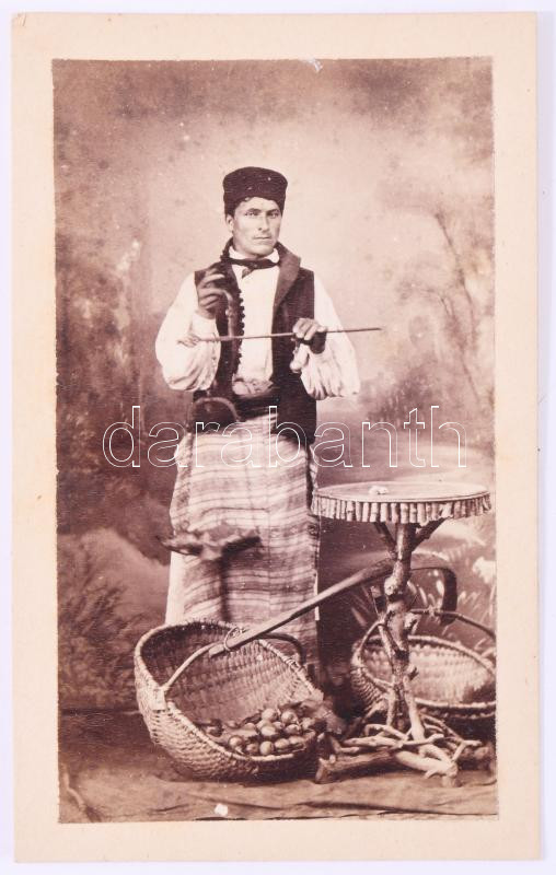 ca 1870 Román gesztenyeárus. Vizitkártya fotó C. Szathmari bukaresti műterméből. 9x6 cm /  ca 1860 Romanian chestnut vendor CDV photo from C. Szathmari's studio in Bucharest. 9x6 cm   Szathmári Papp Károly -  Carol Popp de Szathmári, (1812-1887): Erdélyi származású festő és fotográfus, a kelet-európai fotótörténet egyik legjelentősebb alakja. A világ egyik első haditudósító fotósa (krími háború, 1853-56) Udvari fotográfus volt Bukarestben, a román fejedelmi és királyi udvar megbecsült alkotója, úttörő szerepet játszott a népviseletek, társadalmi típusok és kelet-európai kultúra fényképes dokumentálásában, Művei ma múzeumokban (pl. Bukarest, Bécs, Párizs) szerepelnek. Szathmari esetében egy ilyen vizitkártya nem egyszerű műtermi portré, hanem tudatosan komponált, dokumentáló jellegű felvétel, amely hidat képez a művészi fotográfia és a korai néprajzi ábrázolás között.  Carol Popp de Szathmári, (1812-1887): A painter and photographer of Transylvanian origin, one of the most significant figures in the history of Eastern European photography. One of the world's first war correspondent photographers (Crimean War, 1853-56). He was a court photographer in Bucharest, a respected artist of the Romanian princely and royal courts, and played a pioneering role in the photographic documentation of folk costumes, social types and Eastern European culture. His works are now in museums (e.g. Bucharest, Vienna, Paris). In Szathmári's case, such a business card is not a simple studio portrait, but a consciously composed, documentary-style shot that forms a bridge between artistic photography and early ethnographic depiction.