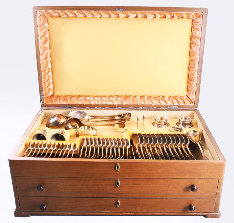 141 darabos ezüst (Ag) evőeszköz készlet, dobozában. Budapest, 1937-1966 közötti fémjel, 800 ezrelékes ezüst, PJ mesterjegy. 2 darab húsvilla nettó 247g - 2 darab szervírozó villa nettó 124g - 12 darab süteményes villa nettó 637g - 12 darab villa nettó 1005g - 12 darab kisebb kés bruttó 657g - 12 darab nagyobb kés bruttó 963g - 12 darab dzsemes kanál nettó 421g - 12 darab halkés nettó 705g - 12 darab halvilla nettó 807g - 2 darab tortalapát nettó 339g - cukorfogó nettó 57g - süteményszervírozó kanál és villa nettó 375g - 12 darab kávés kanál nettó 235g - 12 darab teás kanál nettó 436g - 12 darab evőkanál nettó 1035g - szószos kanál nettó 102g - 2 darab fogpiszkatartó nettó 94g - kakaószóró nettó 87g - 3 darab szervírozókanál nettó 394g - 2 darab fűszerkínáló nettó 104g + üvegbetét - 2 darab fűszerkanál nettó 22g. Készlet teljes bruttó súlya 8765g. Háromszintes, kétfiókos, kulcsokkal zárható tartódobozban, melynek egyik lába hiányzik, 40x63x24 cm.  ///  141-piece silver (Ag) cutlery set, in its original case, bearing 800 fineness hallmarks dated between 1937-1966, with PJ maker's mark. 2 carving forks, net weight 247 g, 2 serving forks, net weight 124 g, 12 pastry forks, net weight 637 g, 12 dinner forks, net weight 1005 g, 12 smaller knives, gross weight 657 g, 12 larger knives, gross weight 963 g, 12 jam spoons, net weight 421 g, 12 fish knives, net weight 705 g, 12 fish forks, net weight 807 g, 2 cake servers, net weight 339 g, sugar tongs, net weight 57 g, pastry serving spoon and fork, net weight 375 g, 12 coffee spoons, net weight 235 g, 12 teaspoons, net weight 436 g, 12 tablespoons, net weight 1035 g, sauce ladle, net weight 102 g, 2 toothpick holders, net weight 94 g, cocoa shaker, net weight 87 g, 3 serving spoons, net weight 394 g, 2 condiment holders, net weight 104 g, with glass inserts, 2 condiment spoons, net weight 22 g. Total gross weight of the set is 8,765 g. The set is housed in a three-tier, two-drawer, lockable storage case with keys; one leg is missing; dimensions 40 × 63 × 24 cm.