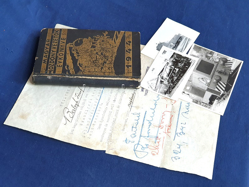 Mozdonyvezetők évkönyve 1944. Budapest, 1943. Mozdonyvezetők Segélyző Egyesülete - Athenaeum Irodalmi és Nyomdai Rt. 264 p. A Mozdonyvezetők Segélyző Egyesülete 1927-ben indította útnak évente jelentkező szakmai és érdekvédelmi kiadványsorozatát, akkor még Mozdonyvezetők zsebnaptára címmel (a kiadvány 1942-ben vette fel a Mozdonyvezetők évkönyve címet). Évkönyvünk a mozdonyvezetők szakmai ismereteinek elmélyítésére, munkavégzésük naplózására és munkaviszonyuk fizetési és társadalombiztosítási részleteinek nyilvántartására szolgált. Néhány szakmai ábrával és számos nyilvántartó táblázattal megjelenő évkönyvünk kiválóan érzékelteti a háborús helyzetet és paranoiát: az éppen közölt tartalomtól függetlenül a szövegoldalak alján olykor markáns parancsok jelennek meg, melyek a rémhírterjesztők és pánikkeltők azonnali szankcionálására szólítanak fel: "Óvakodj a rémhírterjesztőktől és a fecsegőktől!", "Mindenkivel szemben légy bizalmatlan!", "Az ellenség mindent lát, mindent hall. Védekezz ellene!", "A vasút belső ügyeiről idegennek ne adj tájékoztatást", "Idegeneket ne engedj mozdonyod közelébe", "Alig valószínű, hogy kémkedést valakire rábizonyíthass. Ne várj a bizonyítékokra: gyanúdat is azonnal közöld a főnököddel, a hatóságokkal. Ez nem rágalmazás. Ha gyanúd alaptalannak bizonyul, ebből sem rád, sem az illetőre semmi hátrány nem háramlik", "Az elfogott kémgyanús egyént mezítelenre vetkőztesd, és ruháit zárd el, míg a hatóságnak átadhatod", "A kém és szabotáló büntetése: halál!". A kötet végén a MÁV területi egységeinek teljességre törekvő szaknévsora, fűtőházi főnököktől mozdonyvezető tanoncokig. Az előzékeken szakmai hirdetések. Aranyozott, illusztrált, sérült, javított gerincű kiadói egészvászon kötésben. Hozzá tartozik: [Kézirat] Nyílt rendelet Balogh József mérnök úr mozdonyvezetői gyakorlatáról. A Magyar Királyi Államvasukat Budapest-Északi Fűtőházfőnökség által kiadott, bélyegzőjével hitelesített és a fűzőházi vezetőség által aláírt gyakorlati engedély. (1932). Kelt: Budapest, 1932. szeptember 5. Egyetlen levél, 11 gépelt sor, 7 beírt sor, a levél mérete: 295x210 mm. Szövege: "Nyílt rendelet. Balogh József mérnök út a mozdonyvezetői szolgálat begyakorlása céljából van kirendelve. Szabályzót csakis a mozdonyvezető jelenlétében és annak felelőssége mellett kezelhet. Ezen igazolvány, melyet a mozdonyvezetőnek felmutatni tartozik, mozdonyon és vonattal való utazásra jogosít. A mozdonyvezető ezen rendeletemet tudomásul venni és aláírásával ellátni tartozik. Budapest, 1932. szeptember 5-én". A gépelt sorok alatt további kézírásos sorok, a hátoldalon a fűtőház mozdonyvezetői szolgálati beosztása 1932. szeptember 5. és 1932. szeptember 27. közt, mozdonyszámokkal és szolgálatteljesítő aláírásokkal. Hozzá tartozik: [Fotó] A MÁV amerikai gyártmányú, 411-es típusú nehéz tehergőzmozdony-állományának 411.248-as pályaszámú példánya ipari vágányon, vasúti fűtőház előtt. (1960). Vintázs, zselatinos ezüst nagyítás, mérete, mérete: 60x82 mm. Felvételünk hátoldalán a Magyar Közlekedési Múzeum bélyegzője, felvételünk feltehetően egy ismeretterjesztő kiadványhoz készült. Jó állapotú fénykép. Hozzá tartozik: [Fénykép] A MÁV P. F. T. 3103 típusú tehergépvágánygépkocsija ipari vágányon, vasúti fűtőház előtt (1960). Vintázs, zselatinos ezüst nagyítás, mérete, mérete: 52x54 mm. A felvétel a hátoldali feliratozás szerint Miskolcon készült. Jó állapotú fénykép. Hozzá tartozik: [Fénykép] A MÁV keletnémet gyártmányú, A26-os típusú dízel-hidraulikus tolatómozdony-állományának A26-062-es pályaszámú példánya ipari vágányon, vasúti melléképület előtt. (1970). Vintázs, zselatinos ezüst nagyítás, mérete, mérete: 82x114 mm. Feliratozatlan felvételünk az előbbi két fotónál később készült, a VEB Lokomotivbau Karl Marx 1968 és 1976 között gyártotta az A26-os típusú tolatómozdonyokat a keleti blokk vasútjai számára. Jó állapotú fénykép.