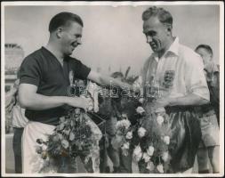 1954 Magyarország-Anglia, a legendás 6:3-as labdarúgó mérkőzés visszavágója, ahol ismét a magyarok győztek, ezúttal 7:1-re. A mérkőzés kezdetekor készült eredeti sajtófotó melyen a két csapat kapitánya, Puskás Ferenc és Billy Wright csokrot adnak egymásnak. Pecséttel jelzett, feliratozott sajtófotó, a felső sarkán egy halvány hajtásnyommal 25,5 x 20,5 cm /  1954 Hungary - England, return match of the legendary football match 6:3. In this return match also the Hungarian Golden Team won (7:1). Official press photo at the begining of the match where the two captains Puskas and Wright exchange bouquets. Slght fold mark. 25,5 x 20,5 cm
