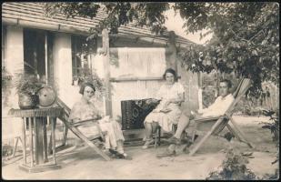 cca 1925 Szőnyegszövő hölgy az udvaron társaságban pihenés közben, pecséttel (Szremcsányi M.) jelzett fotólap, 9×14 cm