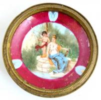 Porcelán berakásos réz tányér, antikizáló grafikával a porcelánon, részben kézzel festett, jelzés nélkül, a porcelánon kopásnyommal, repedésekkel, d: 10 cm