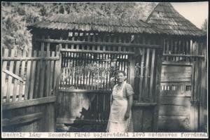 cca 1930 Székely lány Homoródfürdő bejáratánál lévő szénsavas forrásnál, feliratozott fotó, 11×16,5 cm
