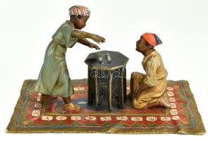 Perzsaszőnyegen kockázó arab gyermekek. Öntött, patinázott és kézzel festett bécsi bronz. Korának megfelelő kopásokkal. Jelzés nélkül. XX. sz. 15,5x9,5x8,5 cm. A bécsi bronz (Wiener Bronze), bronzból készült kisplasztikák gyűjtőneve, amelyeket a 19. század végén és a 20. század elején számos bécsi öntödében készítettek. Különösen a Gründerzeit (Tágabb értelemben a Gründerzeit a Német Birodalom és Ausztria-Magyarország 19. századi gazdaságtörténeti szakaszára utal, amely a széles körű iparosodással kezdődött és a Gründerkrach-ig (az 1873-as nagy tőzsdekrachig) tartott.) idején váltak híressé a vonatkozó miniatűr bronzok, mint dísztárgyak. A bécsi bronzfigurák tematikája leginkább erotikus jelenetekre, távoli kultúrák (keletiek, indiánok, mórok) emberalakjaira és fantáziadús állatábrázolásokra összpontosít.