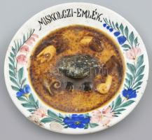 Miskoczi-emlék, kézzel festett kerámia tányér, öblében, kocsonyában ülő béka. Sérült, jelzett: Körmöcbánya, d: 14,5 cm. ,,Pislog, mint a miskolci kocsonyában a béka