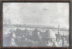 Zeppelin léghajó Budapest felett, 1931. Vintage fotó, sérült. Jelzés nélkül. Üvegezett fakeretben, hátoldalán Hoffmann Ferencz budapesti képkeretező korabeli címkéjével. 17×23 cm