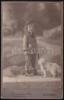 cca 1900 Vadásznak öltözött kisfiú, kutyával, játékpuskával, szájában pipával; keményhátú kabinetfotó a Brenner Testvérek szegedi műterméből, 16,5x10,5 cm