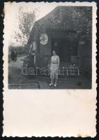 1941 Vámfalu, Erdély, Szatmár megye, Maksay Piroska postahivatalnok a posta épülete előtt, hátoldalán feliratozott vintage fotó, jobb felső sarkában apró foltokkal, 8,5x6 cm