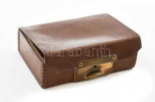 Régi bőr mandzsetta tartó dobozka, gombnyomásra nyíló, működő zárral. Jelzett: Csángó Budapest IV., Múzeum körút 5. Korának megfelelő állapotban, 10x7x3 cm. Benne különféle mandzsetták (közte gyöngyház), 2 db gomb, 2 db miniatűr muránói üveg figura.
