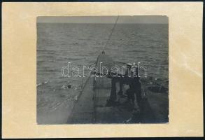 1917. 06.19. Az Osztrák-magyar haditengerészet S.M. U-IV tengeralattjárója a francia Edouard Corbiere hajóra tüzel a hátoldali felirat szerint. Ezen a napon a tengeralattjáró még két hajót süllyesztett el, a francia Cefirát és a görög Kerkyrát. 9x8 cm kartonon /  Original black-and-white photograph pasted onto a postcard-sized piece of cardboard. According to the writing on the back, it purports to show two crewmembers of S.M. U-IV firing the submarines cannon to sink the 475-ton French steamer Edouard Corbiere on June 19, 1917, off Gallipoli in the Gulf of Taranto. The Edouard Corbiere, launched in 1907, had been a passenger ship before being requisitioned as an auxiliary patrol vessel by the French Navy. S.M. U-IV scored three kills on that day: the French Cefira and the Greek Kerkyra.9x8 cm on cartboard