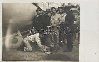 Az S.M.S. Babenberg osztrák-magyar hadihajó matrózai. Egyik büntetőmunkán, miközben a többi tengerész és őrök nézik. / A sailor on his knees brushes a dirty overall on deck under the watchful gaze of two guards armed with rifles and bayonets. A group of crew members watches, apparently not greatly concerned or impressed by the scene. Probably the kneeling sailor was under arrest and being forced to do this sort of work. .Black-and-white photo postcard