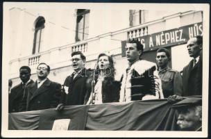 cca 1950 Szocialista rendezvény, "Hűség a néphez, hűség a párthoz" felirattal, a tribünön jelmezt viselők, katona, fekete férfi. Fotó, 14x9 cm