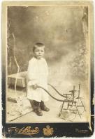 cca 1915 Kisfiú portréja tolószékes játékkal, keményhátú fotó, Ploesti (Ploiesti), Friedrich A. Brand, kopott, kis foltokkal, 16x11 cm / cca 1915 Portrait of a little boy with wheelchair game, board photo, Ploesti (Ploiesti), Friedrich A. Brand, worn, with little spotties, 16x11 cm