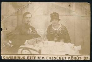 1917 Bp., katonatiszt (Katonai Érdemérem (Signum Laudis) és Károly-csapatkereszt kitüntetésekkel) és hölgy a Gambrinus étteremben (VII., Erzsébet körút 27.), reklámfelirattal ellátott fotólap, viseltes állapotban, saroktöréssel, 9x14 cm