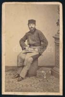 cca 1865 Szőrmesapkát és kötényt viselő férfi, mellette ládával, vizitkártya Simonyi Antal pesti műterméből, kissé foltos, alja vágott, 9x6 cm