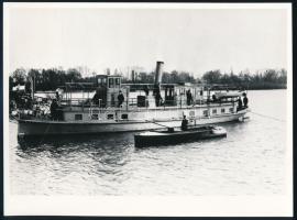 S.M.D. János a Dunai Flottila vontató hajójának használt hajó fényképe későbbi nagyítás 18x14 cm  Black-and-white modern reproduction from an original negative (horizontal, 17.90 cm x 13.2 cm). Full portside view of Janos moored to shore. Several civilians are on deck; a launch has pulled up next to the tugboat, whose name can be read on her bow.