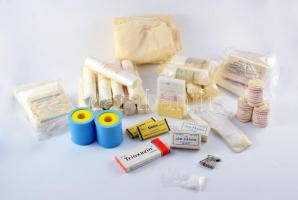 cca 1970 Egészségügyi rajtáska, valószínűleg úttörők által, hadijáték kellékeként használt elsősegély csomag, benne számos tartozékkal: kötszerek (steril géz, mullpólya), Chinoplast tapasz, gyógyszerek (Trioxazin és Dolor tabletta), ampullák, stb. (mind bontatlan); továbbá tartalomjegyzék, üres jegyzetfüzet és ceruza, illetve tartalék öv/szíj. Műbőr táskában, korának megfelelő állapotban, kb. 28x19x23 cm