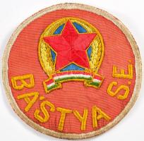 cca 1951-1953 Bástya SE felvarró, d: 10,5 cm  Bástya SE: Az Államvédelmi Hatóság (ÁVH) sportegyesülete, amely 1951-ben alakult, előtte a Budapesti Textiles SE nevet viselte, amely a nagy múltú MTK (Magyar Testgyakorlók Köre) utódja volt. Ezen a néven mindössze két évig működött, 1951 és 1953 között; 1953-tól Budapesti Vörös Lobogó SE, majd 1956 után ismét MTK néven szerepelt az egyesület. Az ÁVH vörös csillagos jelvénye látható a felvarrón is.