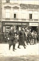 Szombathely, magyar katonák, darutollas cserkészek, Gyógyszertár a Szentlélekhez, Jesztl József üzlete. photo  1938 novemberében a szombathelyi frontharcosok Korponay Kreutz Ede vezetésével a Fő térről indultak Felvidék megszállására, november 20-án vonultak be Ungvárra. A képen a Fő tér 9. számú épületet láthatjuk, ami Jesztl-házként is ismert. Az 1920-as évektől egészen a közelmúltig itt volt a Jesztl család lakása, szűcs műhelye és üzlete.  //  In November 1938, the Hungarian troops from Szombathely, led by Ede Korponay Kreutz, set off from the Main square to get back Upper Hungary, and entered Uzhorod on November 20. The picture shows building number 9 on Main square, also known as Jesztl House. From the 1920s until recently, this was the home, furrier's workshop and shop of the Jesztl family.